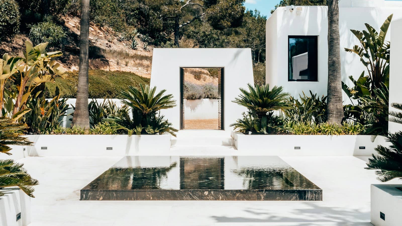 Witte villa met palmen, een poort naar de heuvels en een spiegelvijver